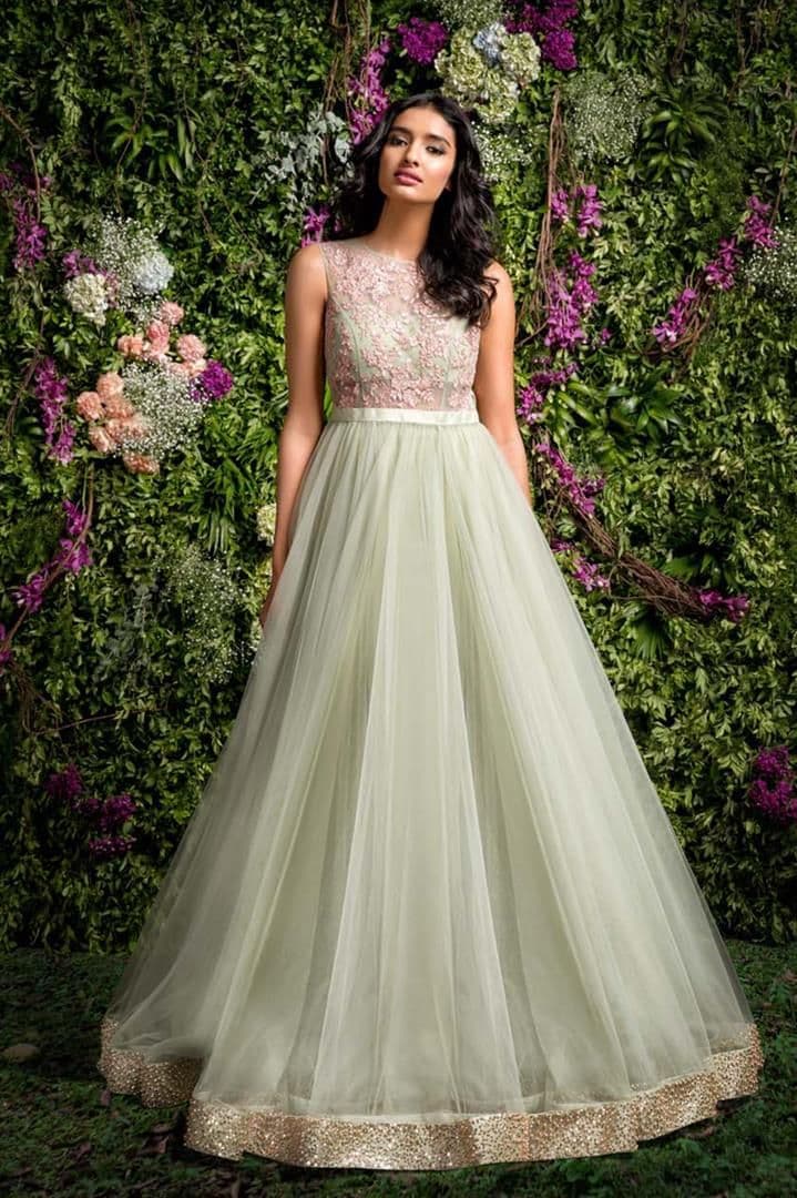 Model wearing a mint green tulle gown with a pink floral embroidered bodice and gold border